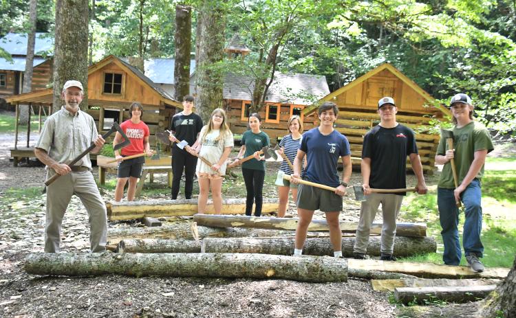 Megan Broome/The Clayton Tribune. Local students participate in the Foxfire Summer Leadership Program and help Foxfire Museum Director Barry Stiles hew logs to prepare building the miniature replica Blacksmith Shop that will be featured at The Children’s Village. Pictured are Stiles; Rabun County High School students Luke Thompson, Sam Flaherty, Celton Littrell, Sean Flaherty, Brinn Justice, and Gavin Sharpe; Rabun Gap-Nacoochee School student Lily Karplus; and home-schooled student Olivia Nixon. 