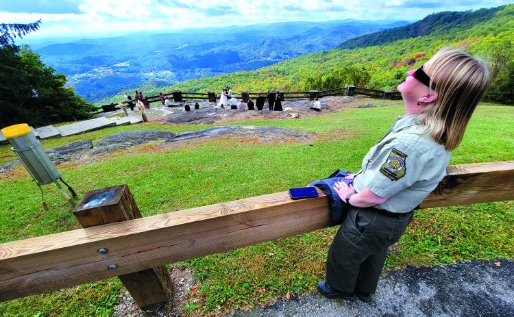 Enoch Autry/The Clayton Tribune. Jessica James-Weeks, the manager of Black Rock Mountain State Park, gazes toward the sky while wearing her special glasses to view the solar eclipse on Oct. 14. In the background, Garrett McClure and Taylor Herrington say their vows in the Blue Ridge Mountains.